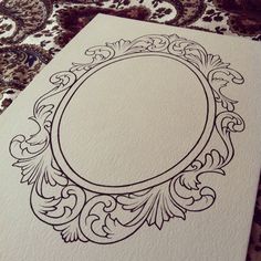 a white card with an ornate frame on the front and back side, sitting on a patterned tablecloth