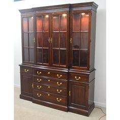 a large wooden china cabinet with glass doors and gold hardware on the bottom, sitting in a room