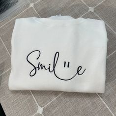 Smile Embroidered Sweatshirt. Hello there! Please message me if you have any additional questions or want to change thread colors. We are a family-run Etsy page; my husband and I make all orders from home. You can also send us a message if you would like a custom sweatshirt/t-shirt with whatever words and images, and we will see if we can accommodate your order! HOW TO ORDER - Please Choose the SIZE and COLOR From Drop Down Menu. MATERIAL - We use JerZees as our blanks; I may sometimes substitut Cute White Sweatshirt For Everyday, White Letter Embroidery Sweatshirt For Loungewear, White Sweatshirt With Letter Embroidery For Loungewear, Everyday White Tops With Letter Embroidery, Funny White Sweatshirt With Text Print, White Sweatshirt With Letter Embroidery, White Everyday Sweatshirt With Letter Embroidery, White Sweatshirt With Letter Embroidery For Everyday, Winter Smiley Face Crew Neck Sweatshirt