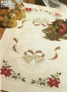 an embroidered tablecloth with bells and flowers on it, next to two vases