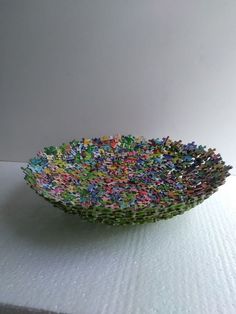 a bowl made out of small pieces of paper on top of a white tablecloth