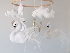 there is a white swan mobile hanging from the ceiling with feathers and clouds on it