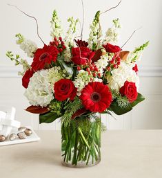 a vase filled with red and white flowers on top of a table next to cookies