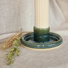 a green candle holder sitting on top of a table next to a stalk of wheat