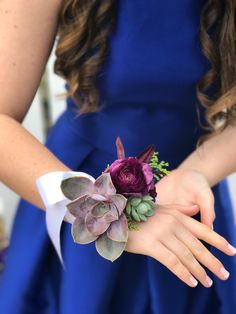 a woman in a blue dress holding a purple flower and succulent boutonniere