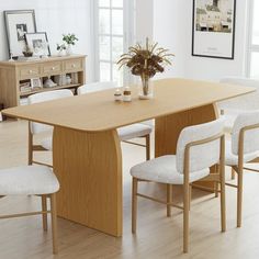 a dining room table with white chairs and a plant in a vase on the end