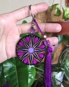 a hand holding a purple and pink keychain with a flower design on it