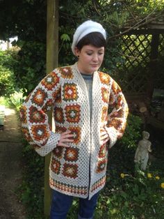 a woman standing in front of a tree wearing a crocheted jacket