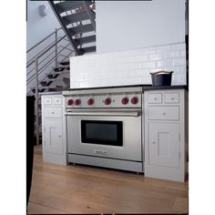 a stainless steel oven in the middle of a kitchen with white cabinets and stairs above it