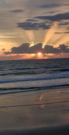 the sun is setting over the ocean with clouds in the sky and waves on the beach