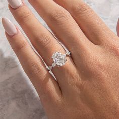 a woman's hand with a diamond ring on top of her finger and the other hand holding an engagement ring