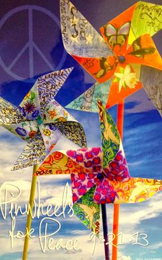 three colorful pinwheels with peace written on the top and bottom, in front of a blue sky