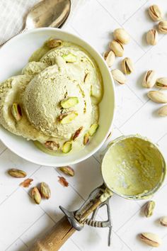 a bowl filled with ice cream next to spoons and nuts on a white table