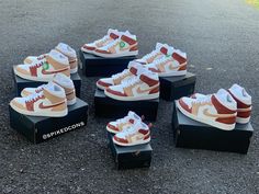 six pairs of sneakers are on display in the middle of an asphalt area, with one pair painted orange and white