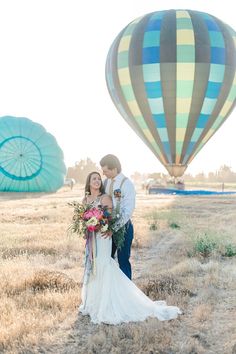 a bride and groom standing in front of hot air balloons