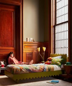 a person sitting on a bed in a room with wood paneling and large windows