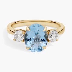 an oval blue topazte ring with three diamonds on the sides and a yellow gold band