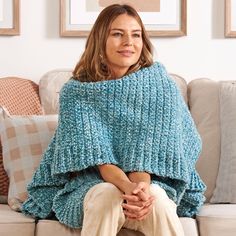 a woman sitting on top of a couch covered in a blue knitted shawl