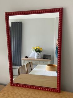 a red framed mirror sitting on top of a wooden table next to a white wall