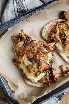 an open faced sandwich with mushrooms and cheese on it sitting on a piece of parchment paper