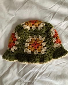 a crocheted green hat with orange and white flowers on it sitting on a bed