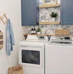 a washer and dryer in a small laundry room with blue cabinets, hanging towels, and potted plants