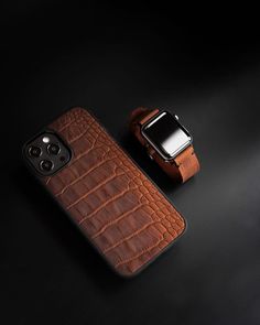 an apple watch and brown leather case on a black surface with a cell phone in the background