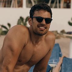 a shirtless man in sunglasses sitting on a beach chair