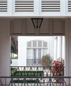 an open door leading to a white building with red flowers in the foreground and green grass on the other side