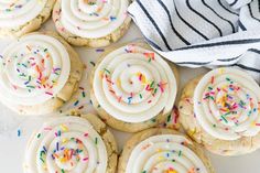 white frosted cookies with colorful sprinkles on a marble countertop next to a black and white towel