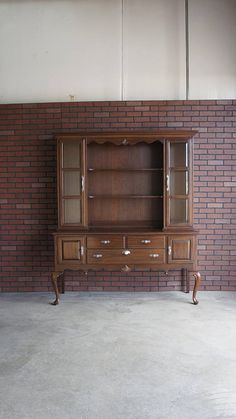 an empty room with a brick wall and wooden furniture on the floor, including a bookcase