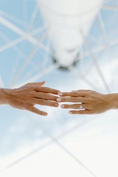 two hands reaching out towards each other in front of a blue sky and white structure