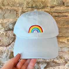 Introducing our Embroidered Rainbow Motif Cap - a vibrant and stylish accessory to add a pop of color to your wardrobe! Available in classic Black, Navy, cheerful Pink, and soothing Pale Blue, this cap offers a delightful selection of hues to match your personal style. The centrepiece of this cap is the expertly embroidered rainbow motif on the front, showcasing a burst of vivid colours that radiate positivity and inclusivity. It's not just a cap; it's a statement of love, unity, and pride. This relaxed and unstructured 'dad cap' style is designed for comfort and versatility, making it the perfect choice for everyday wear. Its soft, adjustable strap ensures a comfortable fit for all head sizes, while the pre-curved brim adds a touch of classic charm. Crafted from high-quality materials, it Casual Adjustable Rainbow Hat, Casual Rainbow Hat, One Size Fits Most, Casual Rainbow Hat One Size, Casual Rainbow Hat One Size Fits Most, Trendy Multicolor Cotton Baseball Cap, Multicolor Cotton Snapback Baseball Cap, Multicolor Snapback Baseball Cap In Cotton, Cute Multicolor Cotton Hats, Casual Multicolor Hat With Embroidered Logo