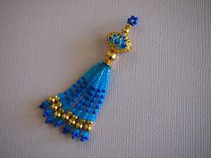 a blue beaded tassel hanging from a gold plated metal hook on a white surface