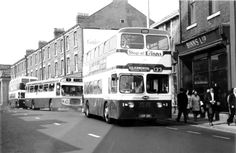 two double decker buses are parked on the side of the street as people walk by