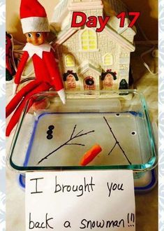 an elf is sitting in front of a glass tray with a sign on it that says, i brought you back a snowman