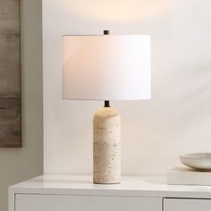 a white table lamp sitting on top of a white dresser next to a bowl and plate