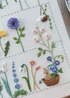 a close up of a piece of embroidery on a table with flowers and plants in it