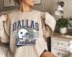 a woman sitting on top of a bed wearing a sweatshirt with the word dallas football printed on it