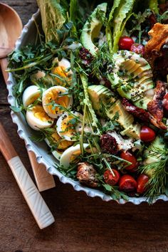 a salad in a bowl with eggs, tomatoes and other vegetables next to a wooden spoon