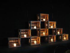 several wooden crates with lit candles on them in the dark, set against a black wall