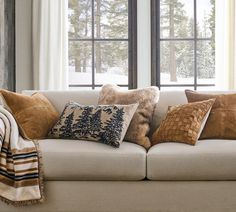 a couch with pillows and blankets on it in front of two large windows that look out onto the woods