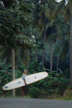 a woman holding a surfboard on the side of a road in front of palm trees