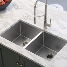 two stainless steel sinks in a kitchen with marble counter tops and gray cabinets, under a faucet