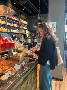 a woman standing in front of a counter with lots of pastries on it and looking at her cell phone