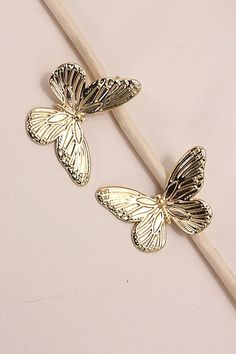 two gold butterflies sitting on top of a wooden stick