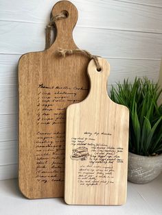 two wooden cutting boards with writing on them next to a potted plant in a vase