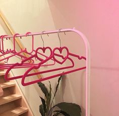 there is a pink rack with heart shaped hangers next to a potted plant