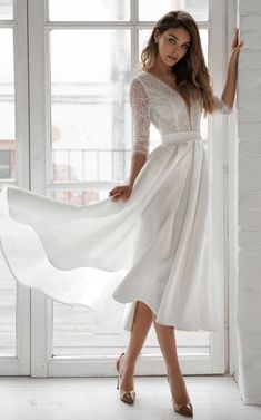 a woman in a white dress standing by a window