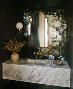 a bathroom with marble counter top and green tile on the wall, along with a vase filled with flowers